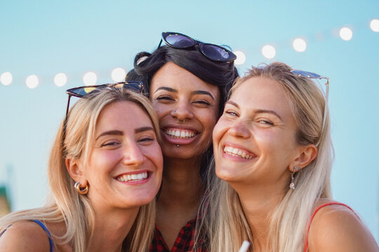 Portrait of three teenagers looking at camera laughing. Young multiracial women having fun on vacation