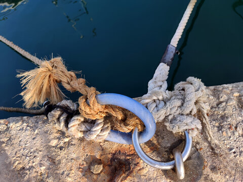 Thick straw rope knotted around metal loops that keep boats tied