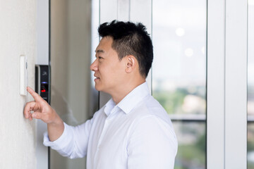 Naklejka na ściany i meble Asian man uses a door knocker with a video camera to open the door.