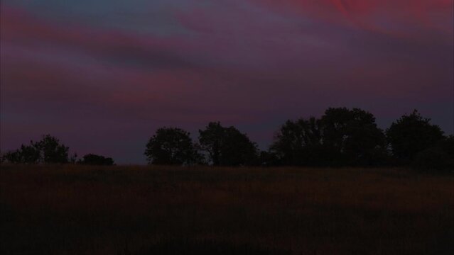 Pink purple and blue sun setting sky in timelapse. UK Somerset countryside time lapse across a field with trees in the distance as the sun sets.