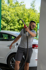 A young man pours gasoline into the gas tank of a white car.A young man pumps gasoline into a gas...