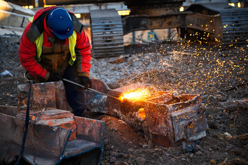 Worker in helmet cuts old metal beam for recycling at site