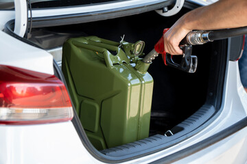 A young man pours gasoline into the gas tank of a white car.A young man pumps gasoline into a gas...
