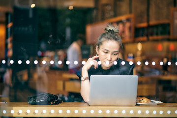 asian business woman sitting by the window in coffee shop working using laptop computer