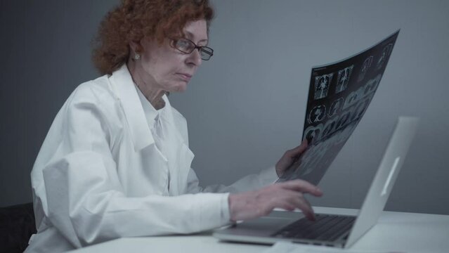 Female radiologist describes patients tomography results by typing on laptop while sitting in hospital. Physician radiographer reviews MRI scans, medical test, and diagnosis. Medicine and health care