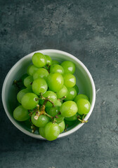 Bowl of green grapes isolated on grey background with copy space. Top view. Shooting in the dark. Place for writing.