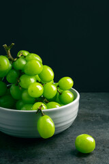 Bowl of green grapes isolated on black background with copy space. Close up view. Shooting in the dark. Place for writing.