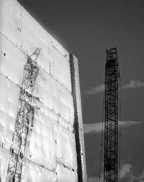 Construction Shadow, Tall Crane Reflected On Side Of Building Wrapped In White Protective Plastic Shrink Wrap