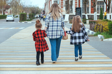 mother took her children by the hands and teaches them to cross the road correctly and safely along...