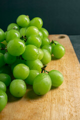 Fresh Green grapes on a wooden cutting board. Shooting in the dark. Close up view. Bunch of grapes on a wooden grey background. Space for writing. Suitable for summer.