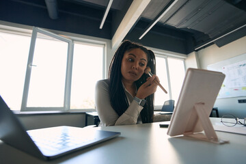 Concentrated office worker putting on makeup before cosmetic mirror