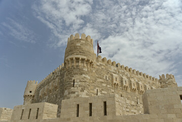 Citadel of Qaitbay, Alexandria, Egypt with the Egyptian flag on top and a background of blue cloudy sky. The Fort of Qaitbay is a 15th-century defensive fortress located on the Mediterranean sea coast