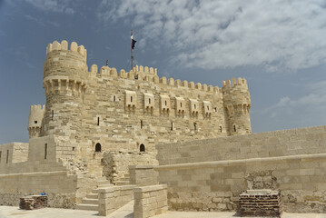 Citadel of Qaitbay, Alexandria, Egypt with the Egyptian flag on top and a background of blue cloudy sky. The Fort of Qaitbay is a 15th-century defensive fortress located on the Mediterranean sea coast
