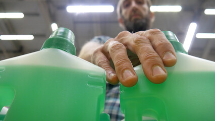 Close-up of plastic bottles with green cleaning agent and a male buyer takes one