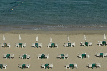 Arrangement of umbrellas, tables, and chairs on a sandy beach in Alexandria, Egypt, on the mediterranean sea. Background of sea waves.