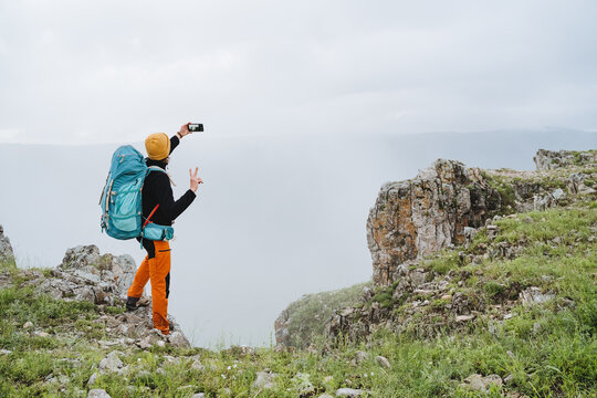 A man with a backpack on his back takes a selfie in the mountains, a guy takes pictures of himself on his phone, a mountain climb to the top, a hike on the rocks