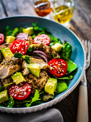 Tasty salad - fried chicken breast, avocado, mini tomatoes and fresh green vegetables on wooden background
