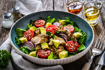Tasty salad - fried chicken breast, avocado, mini tomatoes and fresh green vegetables on wooden...