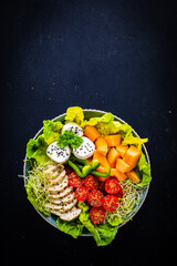 Fresh salad - goat cheese, roast chicken breast, melon and vegetables on wooden table
