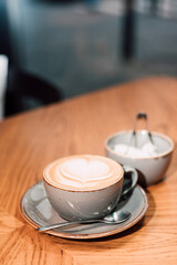 A cup of cappuccino andr efined sugar on a wooden table. 