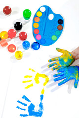 Children's handprints. Blue and yellow palm prints on a white sheet of paper, children's hands in paint, a palette of colorful paints, gouache. Top view of the table. Children's creativity