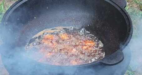 Meat cooking chicken wings on an open fire in a cauldron in boiling oil