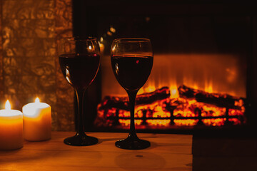 Two glasses wine with candles in front of the fireplace. Romantic atmosphere. Beautiful background with cozy magical composition. 
