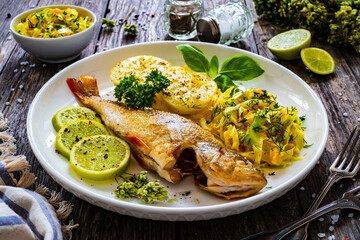 Fried perch with lemon and salad served on wooden table

