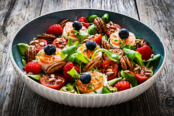 Fresh salad - goat cheese, raspberries, blueberries, pecan nuts, cherry tomatoes, pickled radishes and leafy greens on wooden table
