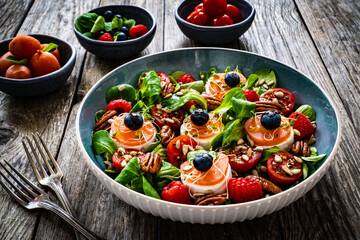 Fresh salad - goat cheese, raspberries, blueberries, pecan nuts, cherry tomatoes, pickled radishes and leafy greens on wooden table
