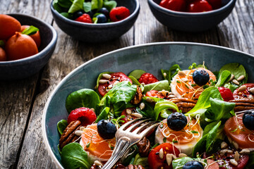 Fresh salad - goat cheese, raspberries, blueberries, pecan nuts, cherry tomatoes, pickled radishes and leafy greens on wooden table
