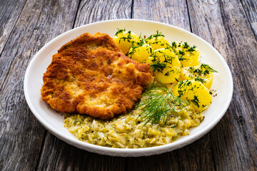 Breaded fried pork chop with bone, boiled potatoes and  boiled cabbage on wooden table
