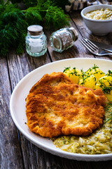 Breaded fried pork chop with bone, boiled potatoes and  boiled cabbage on wooden table

