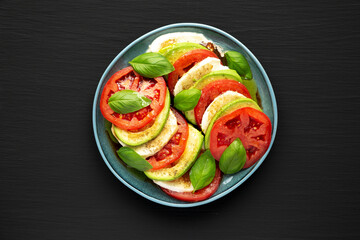 Homemade Organic Avocado Caprese Salad on a Plate on a black background, top view. Flat lay, overhead, from above.