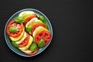 Homemade Organic Avocado Caprese Salad on a Plate on a black background, top view. Flat lay, overhead, from above. Copy space.