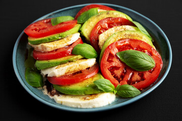Homemade Organic Avocado Caprese Salad on a Plate on a black background, side view.