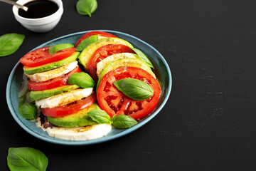 Homemade Organic Avocado Caprese Salad on a Plate on a black background, side view. - Powered by Adobe