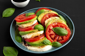 Homemade Organic Avocado Caprese Salad on a Plate on a black background, side view.