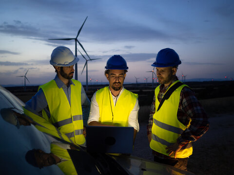 Three male engineers work at night in a field of windmills. Fault, renewable energy
