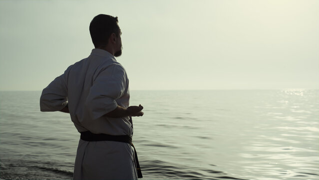 Athletic man honing karate technique enjoying sunset on beach back view - Powered by Adobe