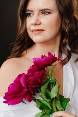 Naklejka premium A peaceful brunette woman in white clothes with a bouquet of peonies.