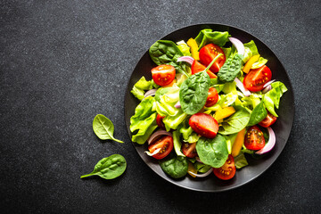 Green salad with fresh vegetables and green leaves at black background. Top view with copy space.