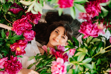 a beautiful and gentle young woman lies in peony flowers. feminine beauty. 