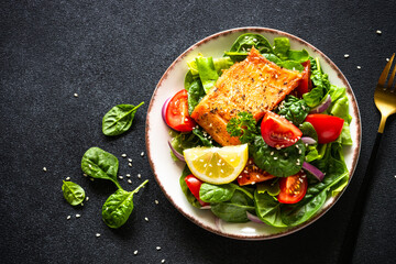 Green salad with salmon fillet. Healthy lunch, diet nutrition. Top view on black.