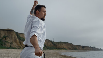 Strong fighter practicing karate on beach closeup. Man training combat exercises