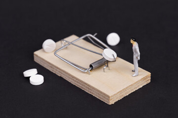 Pharmaceutical trap - a white pill in a wooden mousetrap, next to a human figure on a black...