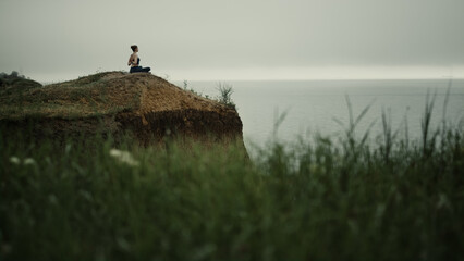 Far view yoga woman exercising on hill top. Girl meditating sitting lotus pose.