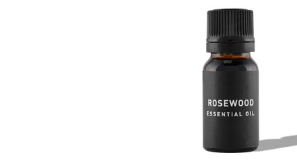 A bottle of rosewood essential oil with shadow on a white background. The idea of natural cosmetic, natural oils, aromatherapy, emotional wellbeing and skincare. Copy space