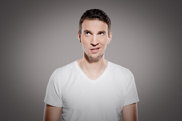 irritated and doltish man with nonsensical face expression look at top corner and show his confused...