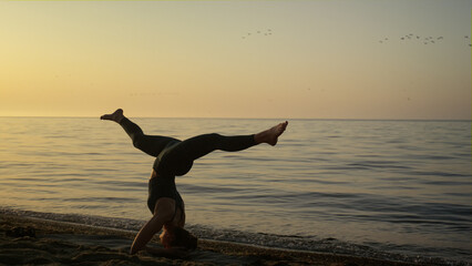Slim girl keeping balance in headstanding outdoors. Yoga woman training on beach